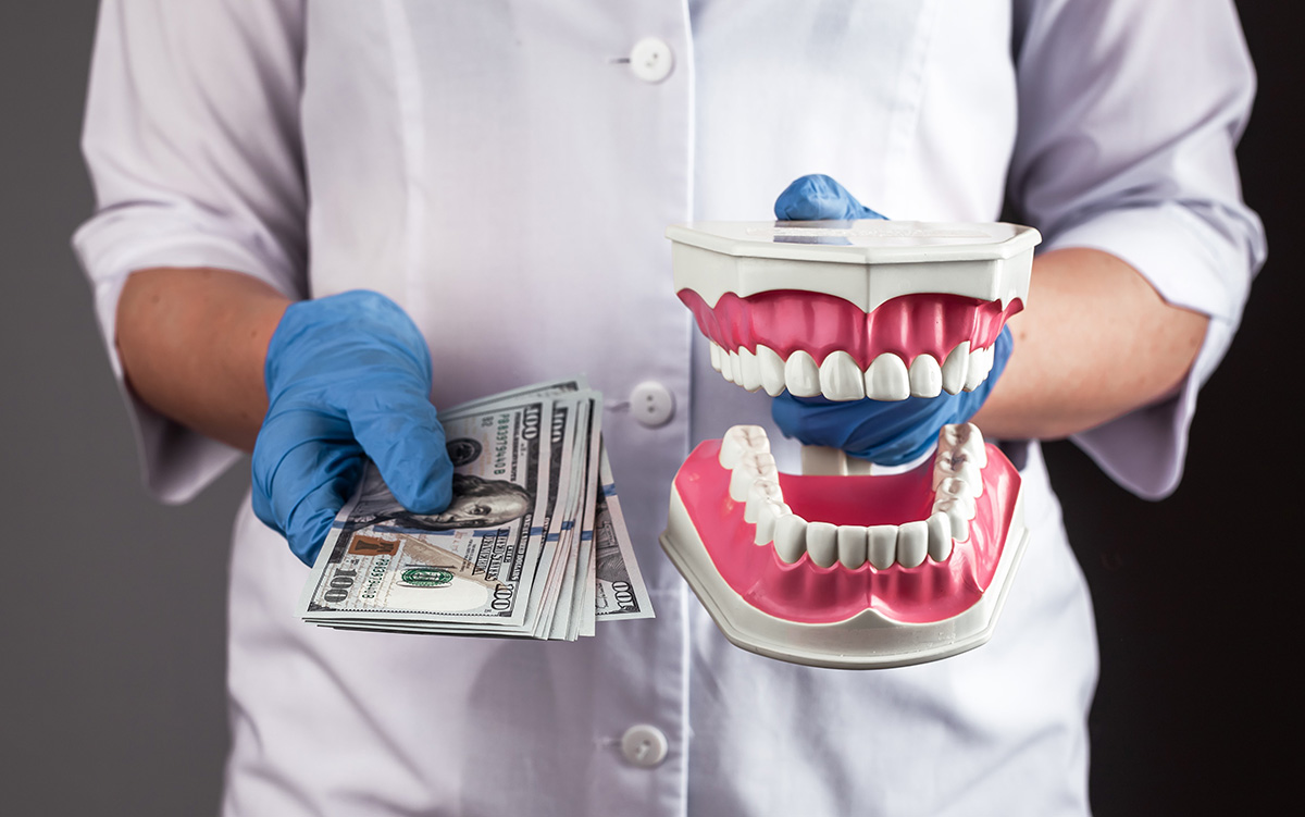 Dental professional wearing blue gloves holding a model of teeth and US dollar bills